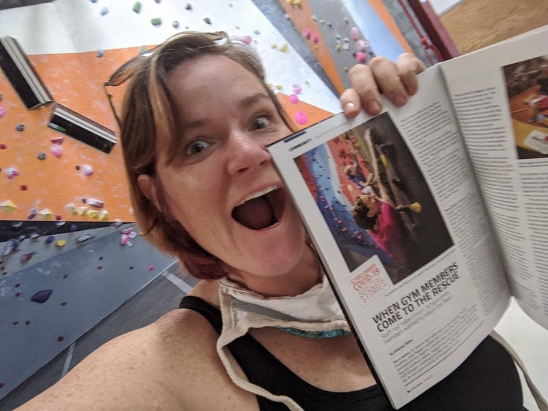 In this photo, we see the female CEO of a climbing gym chain, standing triumphantly in front of a rock climbing wall with a magazine in hand. The magazine features a friend of theirs scaling a seemingly impossible route, their determined expression conveying the intense focus and physical strength required to conquer such a challenge.
 
 As our CEO friend holds the magazine aloft, a mischievous twinkle in their eye suggests that they’re secretly plotting.